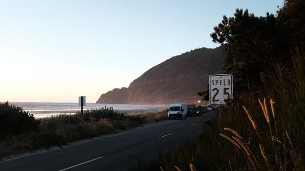 A photograph displaying the iconic Highway 1 in California, with the Pacific Ocean on one side and rugged cliffs on the other. The road is winding and scenic, with a classic convertible car driving along it.