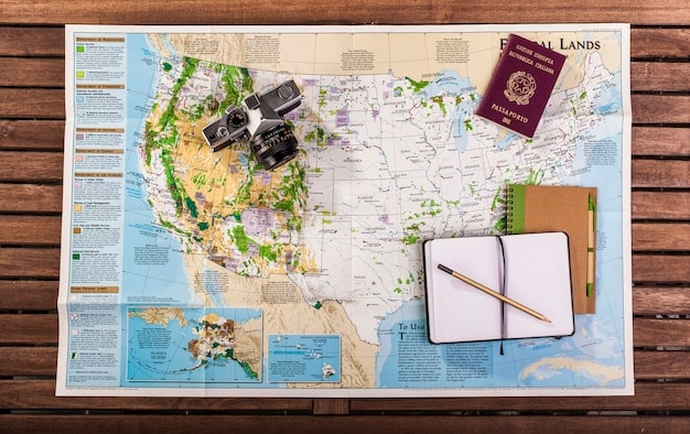 An open map of the United States spread out on a wooden table, along with a compass, a pair of sunglasses, and a travel journal. The map has several routes highlighted, indicating potential road trip itineraries.