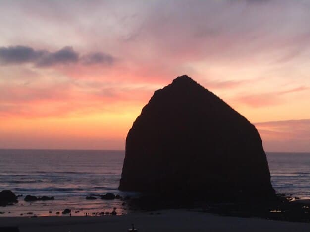 A sunset view of Cannon Beach, Oregon, with the iconic Haystack Rock silhouetted against the colorful sky.