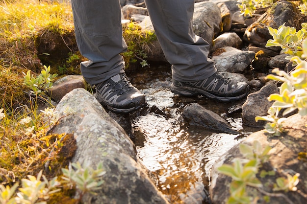 A close-up shot of a hiker wearing waterproof boots navigating a rocky trail alongside a waterfall, highlighting the importance of proper footwear and gear for safety.