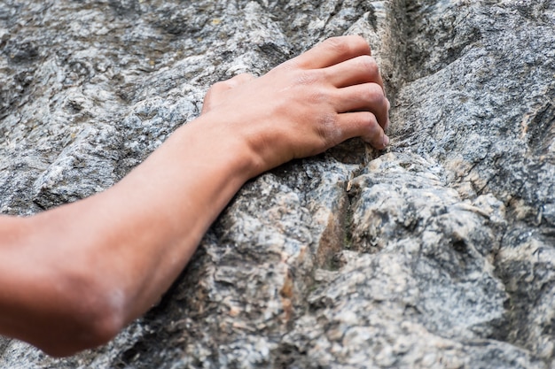 A close-up shot of a climber's hands gripping a textured rock face, chalk dust visible on their fingers. The focus is on the texture of the rock and the climber's determined grip.