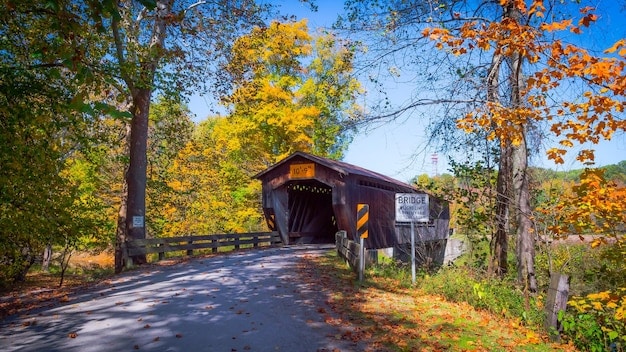 A picturesque covered bridge in Vermont during the fall, surrounded by vibrant autumn foliage and a clear blue sky.