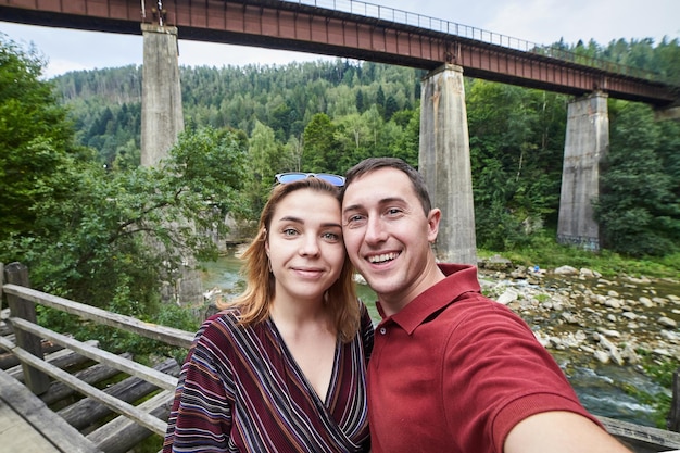 Two travelers smiling and taking a selfie in front of a large train window with a mountain range in the background.