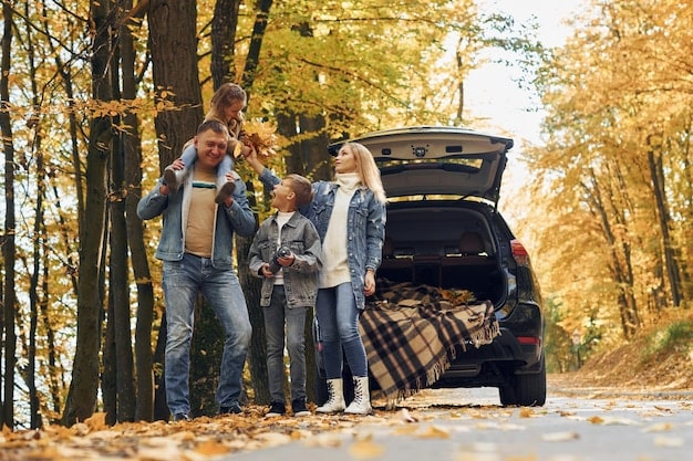A family packing a car with suitcases and gear, ready for a road trip, with a backdrop of autumn leaves.